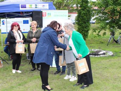 15) Zdjęcie przedstawia Panią Anetę Niestrawską – Sekretarz Gminy Sompolno, która wręcza Seniorce nagrody za udział w konkursach i zabawach zorganizowanych na majówce.