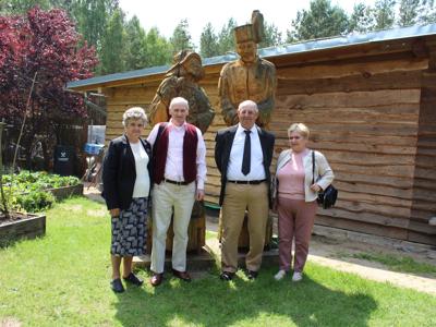 Na fotografii czwórka seniorów pozuje do zdjęcia na tle drewnianych figur