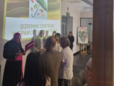 Zdjęcie wykonane w Dziennym Centrum Wsparcia. Przedstawia biskupa oraz przedstawicieli gminy stojących na tle logo placówki.