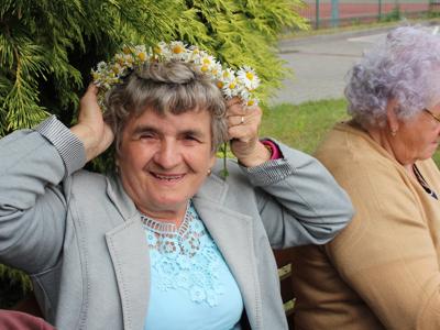 Fotografia przedstawia seniorkę z rumiankowym wiankiem na głowie