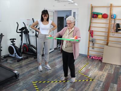 4) Fotografia przedstawia seniorkę podczas konkurencji ruchowej wykonywanej na sali rehabilitacyjnej DDP.