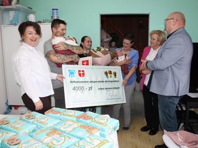 2) Zdjęcie przedstawia moment wręczenia rodzinie dofinansowania na zakup wózka dla trojaczków