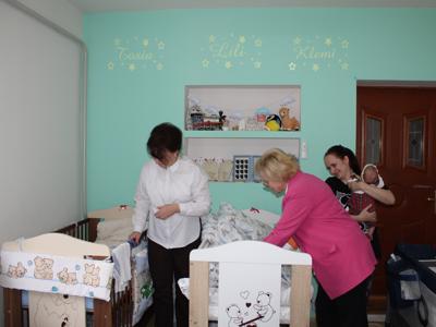 7) Na zdjęciu trzy kobiety stojące przy łóżeczkach dzieci