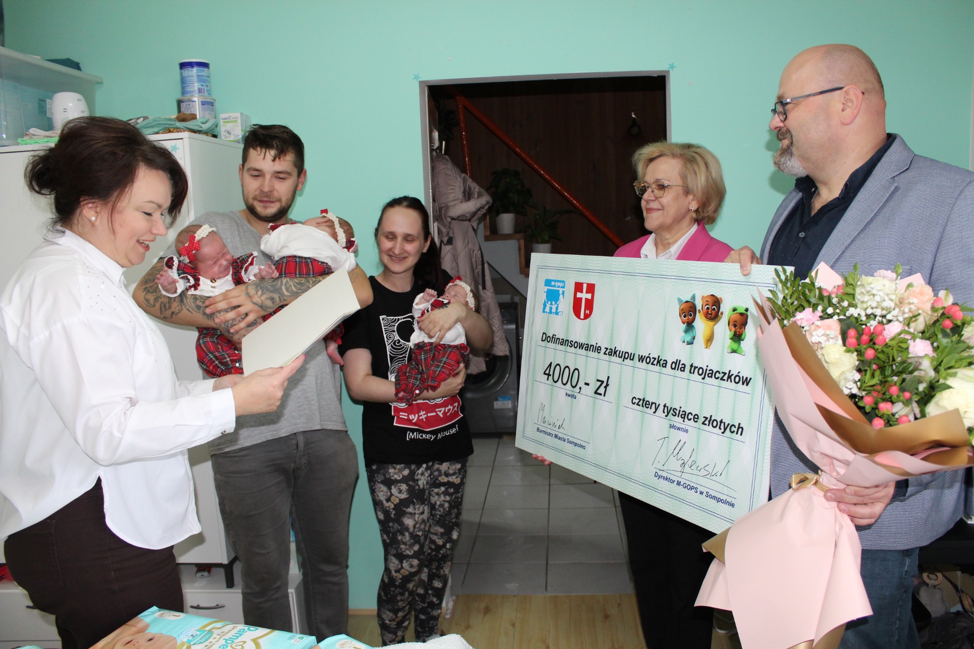 1) Zdjęcie wykonane w domu rodziców trojaczków. Przedstawia rodziców, dzieci oraz przedstawicieli urzędu.