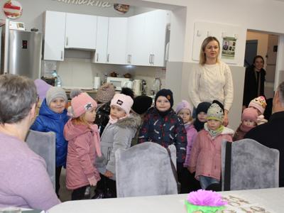 1. Zdjęcie wykonane na sali głównej DDP. Przedstawia przedszkolaków podczas wizyty u seniorów.