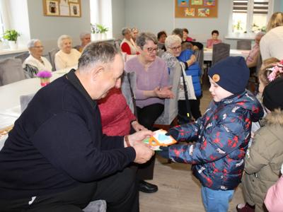 2. Zdjęcie przedstawia chłopca wręczającego seniorowi laurkę