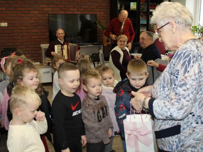 4.  Zdjęcie przedstawia seniorkę wręczającą dzieciom słodki upominek.