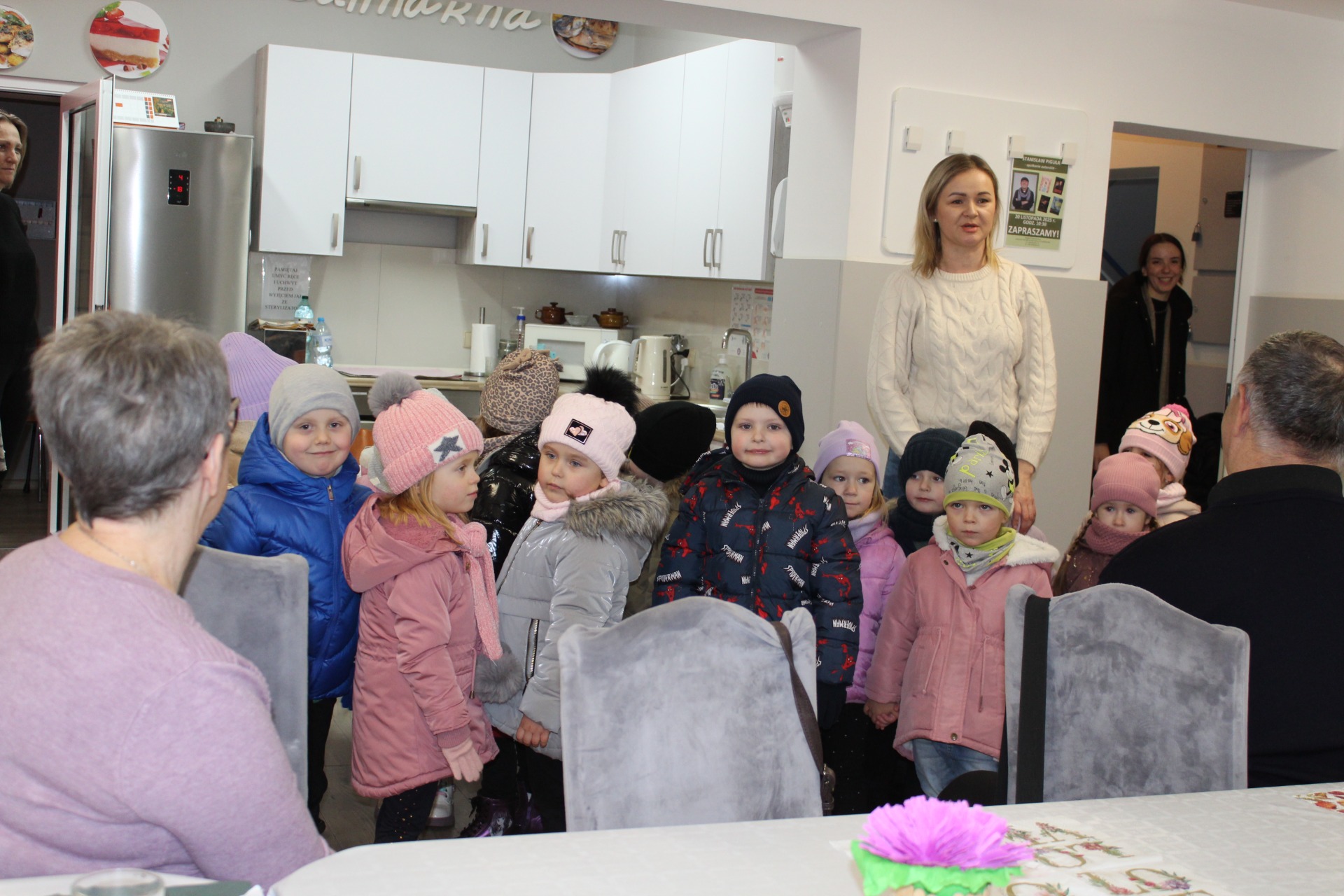 1. Zdjęcie wykonane na sali głównej DDP. Przedstawia przedszkolaków podczas wizyty u seniorów.