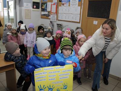 Zdjęcie wykonane w Ośrodku Pomocy Społecznej w Sompolnie. Przedstawia przedszkolaków trzymających dużą laurkę wykonaną z okazji dnia pracownika socjalnego oraz panie nauczycielki.